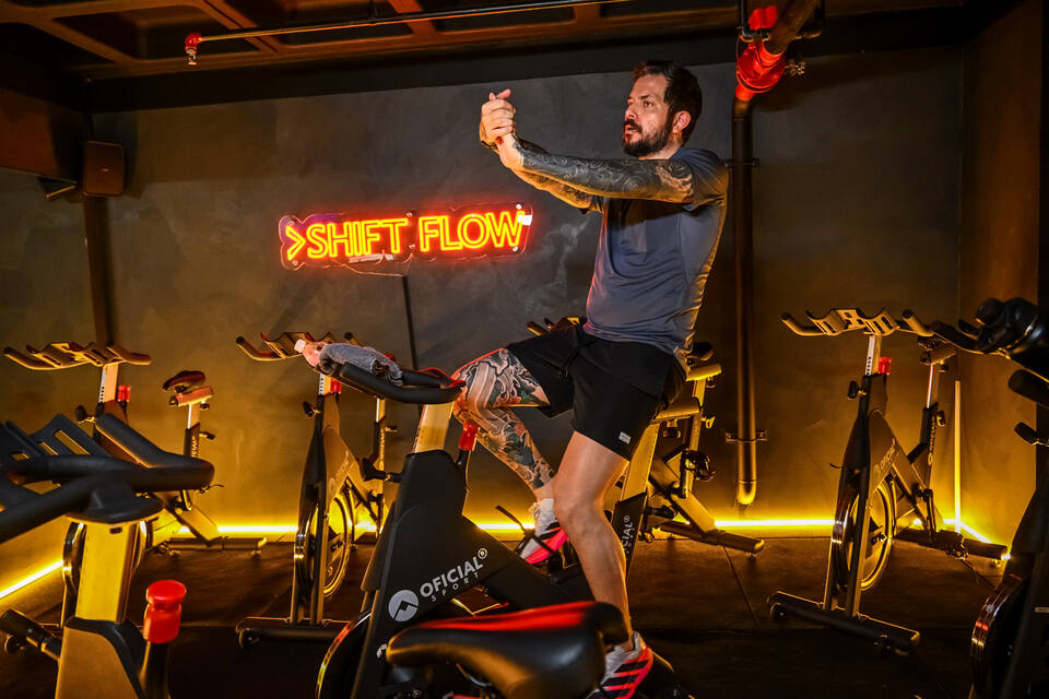 Aluno se alongando na bike do SHIFT Flow, diante do letreiro em neon