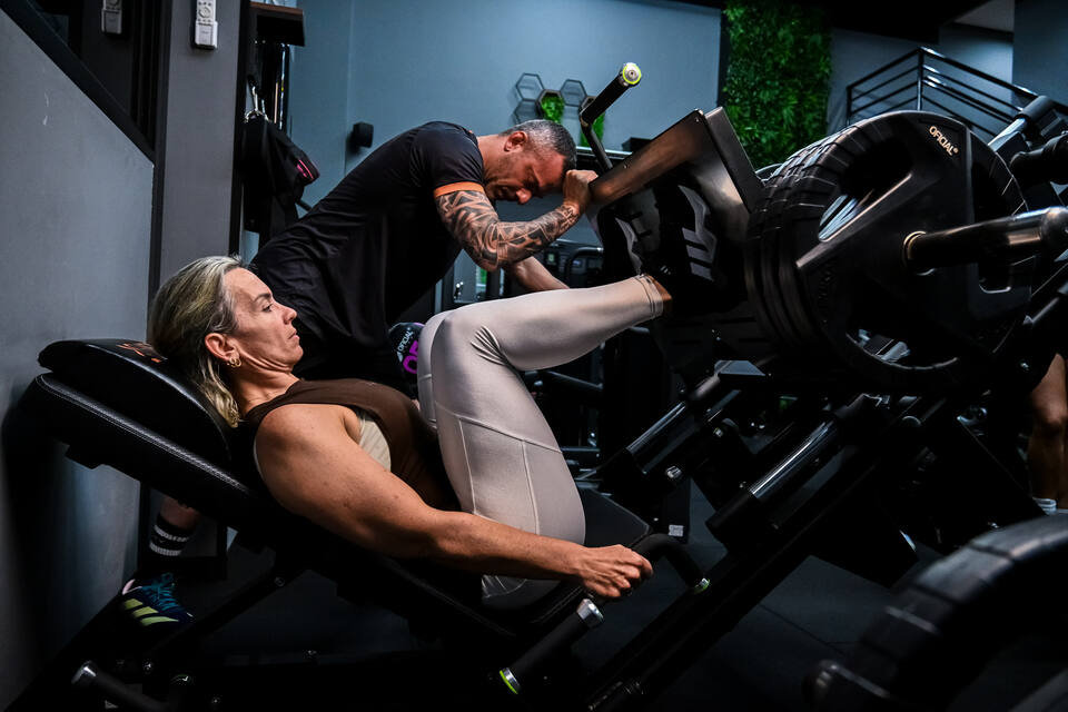 Professor da SHIFT acompanhando a aluna no leg press